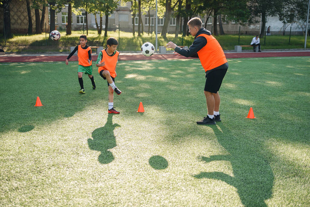 Young soccer coach instructs teen players. A young professional coach trains the ball kicks with young football players. - Photo, image