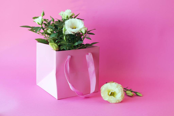 Fresh roses are packed in a pink bag on a light background for a romantic gift - Φωτογραφία, εικόνα