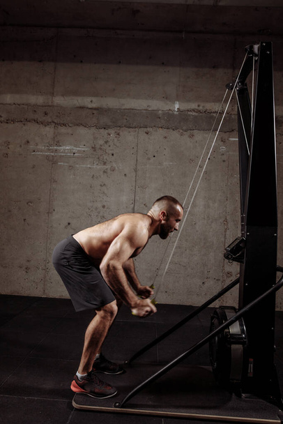 shirtless athlete is pulling the ropes on the equipment in the sport center - Foto, immagini