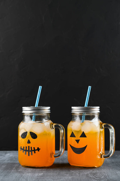 Halloween pumpkin mocktails in glass jars decorated with scary faces on the chalkboard, black background. - Φωτογραφία, εικόνα