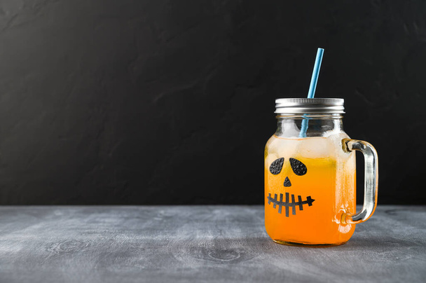 Halloween pumpkin mocktail in glass jar decorated with scary face on the chalkboard, black background. - 写真・画像