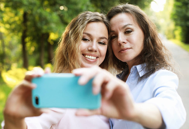 mature mother and adult daughter are doing selfie by mobile phone in summer park - Fotoğraf, Görsel