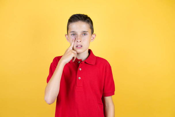 Young beautiful child boy over isolated yellow background Pointing to the eye watching you gesture, suspicious expression - Photo, Image
