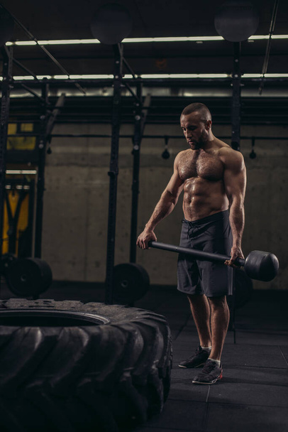 wet , sweaty sportsman is developing muscles with hammer - Foto, afbeelding