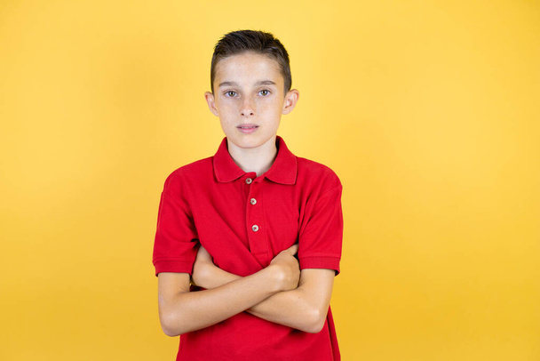 Young beautiful child boy over isolated yellow background serious looking at the camera with cross arms - Photo, Image