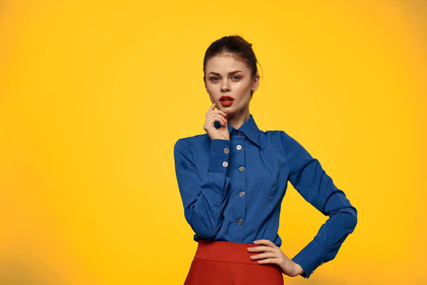 Attractive woman in blue shirt gesturing with her hands and red skirt yellow background portrait cropped view - Photo, Image