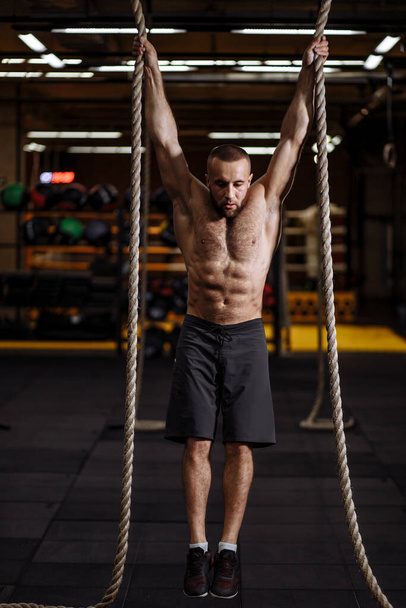 serious young man is concentrated on hanging exercise on ropes - Фото, зображення