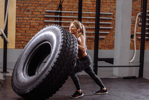 nervous fit female athlete wearing sporty outfit is working out with a huge tire - Valokuva, kuva
