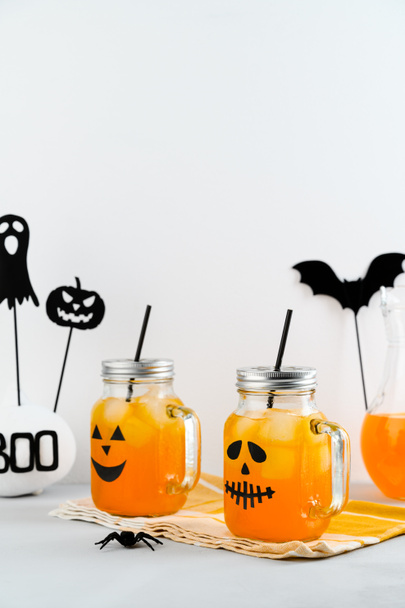 Halloween pumpkin iced mocktails in glass jars decorated with scary faces on a white table. - Photo, Image