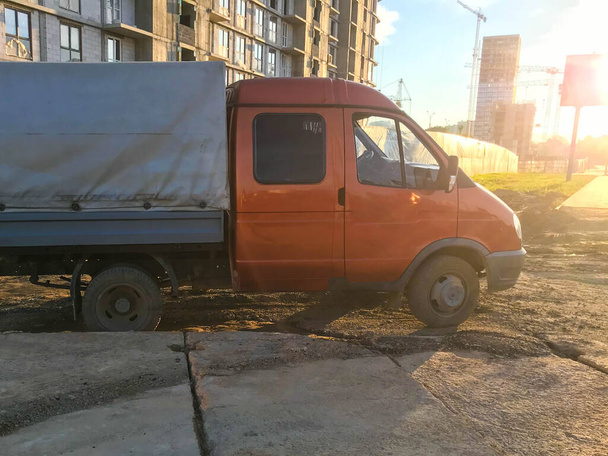egy narancssárga fülkével és szürke bázissal rendelkező teherautó áll a földön. áruszállításra szolgáló kis kerekű autó. építőanyagok, homok és áruk szállítása - Fotó, kép