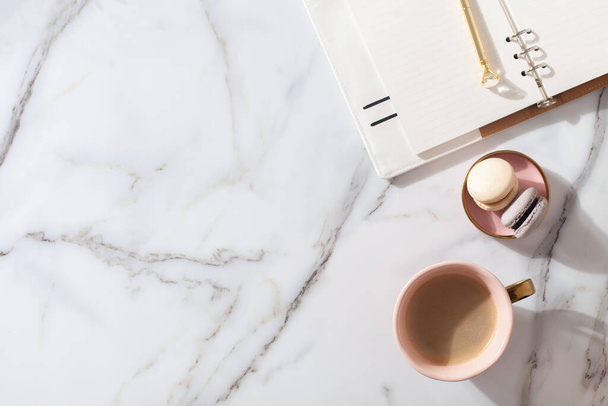 Pink coral colored diary for the year 2021, pen, coffee latte, macaron cookie and straw woven placemat on white marble background. New year planning concept. Minimalistic workstation. Copy space. - Foto, Imagem