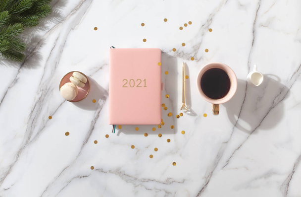 Flat lay composition with coral colored 2021 diary book for writing down New Year's plans, coffee, cookie and mini artificial Christmas trees onside with gold sparkles on white background. Holiday - 写真・画像