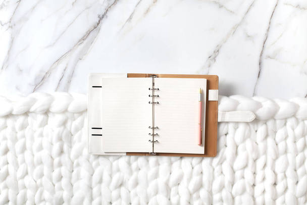 Minimal home workspace with diary, pen, cup of coffee, milk, french macaron and cozy snow white knit cotton plaid. Handmade merino wool chunky knit warm blanket. Flat lay, top view. Organic cotton. - Foto, immagini