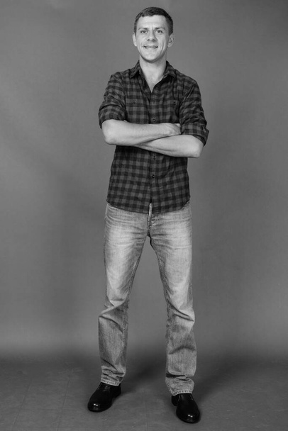 Studio shot of handsome man wearing checkered shirt against gray background in black and white - Fotó, kép