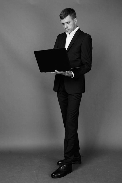 Plan studio d'un bel homme d'affaires portant un costume sur fond gris en noir et blanc - Photo, image