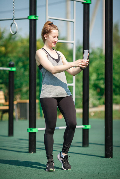 Attractive athletic woman on a street sports field takes a selfie. - Photo, Image