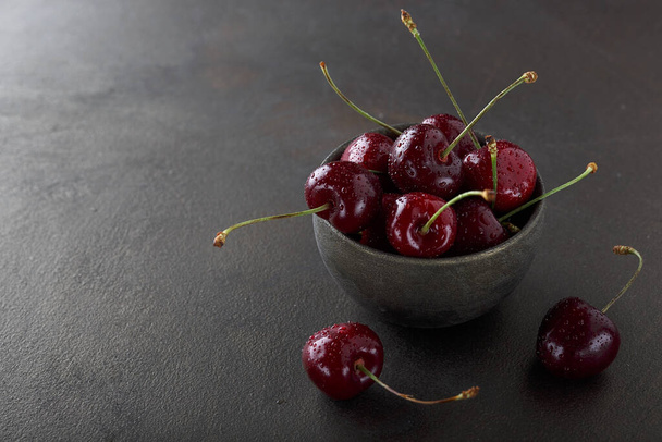 Ripe tasty sweet cherry in an old ceramic bowl on an old table. Dark background. - Photo, Image
