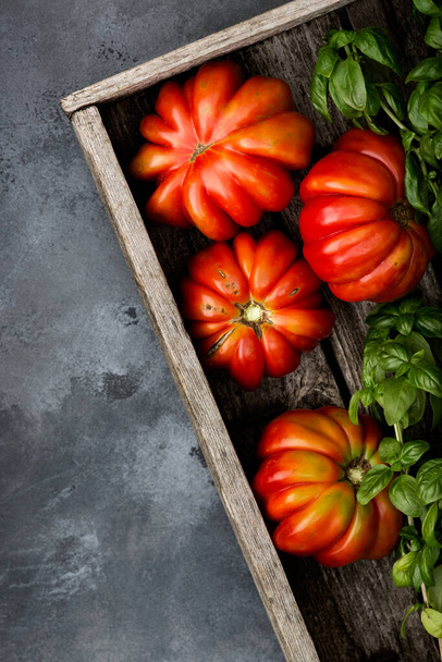 Fresh ripe tomatoes and fresh basil herb in a harvesting box on an old wooden table. Dark background. Top view. - Photo, Image