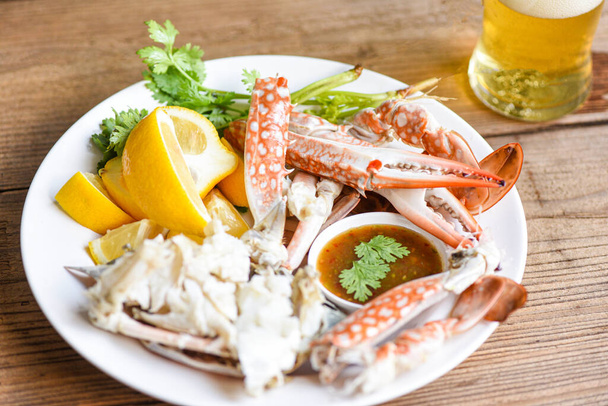 Krabbenfleisch mit Bier / Gekochte Krabbenkrallen und -beine auf weißem Teller und Fischsoße auf dem Tisch, blaue Schwimmkrabbe   - Foto, Bild