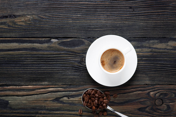 Fresh and aromatic coffee in a white cup and coffee beans on an old wooden table. Top view - Photo, Image