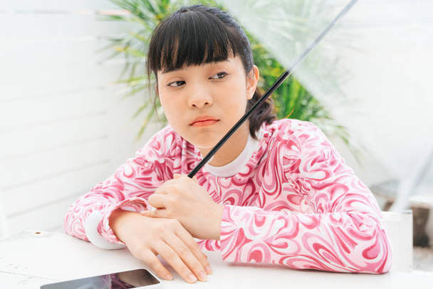 ongelukkige jonge aziatische vrouw in roze shirt met transparante paraplu met smartphone op tafel. - Foto, afbeelding