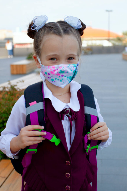 Little school girl wearing uniform and protection mask near the school outdoors. New normal. Coronavirus protection - Foto, afbeelding