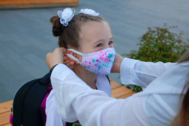Mother is putting on her daughter protection mask before school. Schoolgirl. New normal. Coronavirus protection - Foto, afbeelding