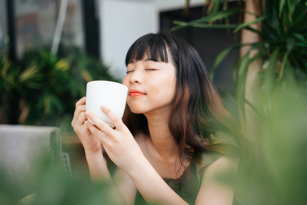 alegre joven asiático mujer disfrutar caliente café en café al aire libre. - Foto, Imagen