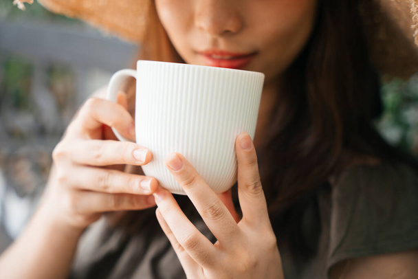 Close up - Young asian woman traveler wearing straw hat enjoy drinking coffee outdoors. - Fotoğraf, Görsel