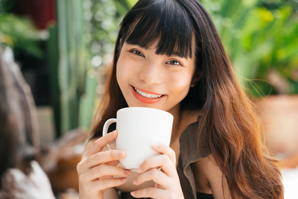 Fröhlich junge asiatische Frau mit einer Tasse Kaffee im Hof. - Foto, Bild