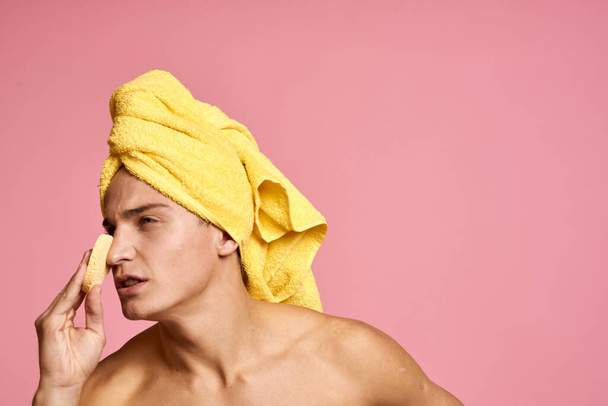 homem com uma toalha na cabeça e uma esponja amarela na mão procedimento cosmético pele limpa do rosto - Foto, Imagem