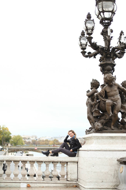 Young woman sitting on Seine bridge near lanterns with sculpture in Paris. - Fotoğraf, Görsel