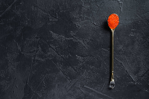 Red caviar in an exquisite spoon. Black background. Top view. Copy space. - Foto, Imagen