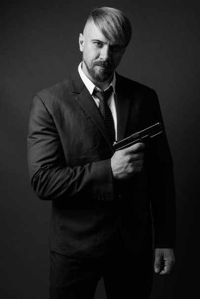 Studio shot of bearded businessman with handgun against gray background in black and white - Photo, Image