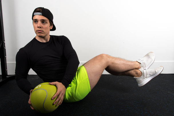 A young fit male exercising and doing the Russian twist with a ball at the gym - Fotoğraf, Görsel