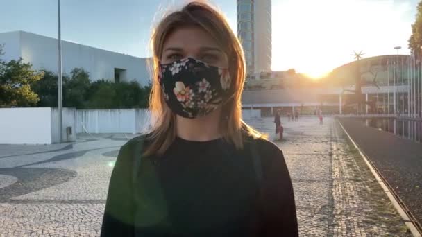 リスボン(ポルトガル)で発生したCovid-19の流行に対して顔マスクを身に着けている若い美しい女性の4kスローモーション映像。後ろに旗竿を持って外を歩く遊び心のある女の子の眺め - 映像、動画