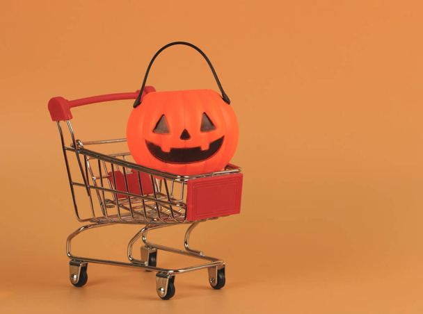 Front view of  Halloween pumpkin on shopping cart  on orange background with copy space. Halloween holiday concept. - Фото, изображение