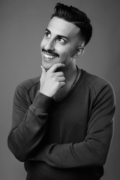 Зйомки молодого вродливого іранського чоловіка з вусами з довгими рукавами сорочки проти сірого фону в чорно-білому - Фото, зображення