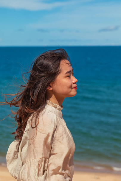 A vertical portrait of a young attractive Asian female model posing at the beach with the sea in the background - Foto, imagen