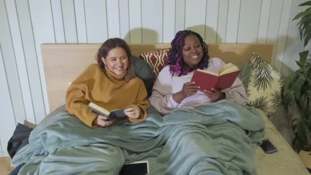 Las mujeres yacen en la cama leyendo libros, ambiente casero, apartamento acogedor en la noche, sonrisa y risa - Metraje, vídeo
