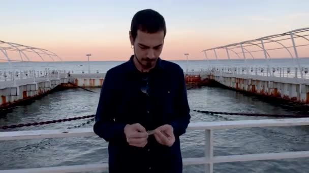 Filmaufnahmen eines gutaussehenden Mannes mit Gesichtsmaske und elegantem dunklen Hemd beim Spaziergang am Ufer des Tejo in Lissabon, Portugal. Mann mit schwarzer Maske gegen die zweite Welle der Covid-19 - Filmmaterial, Video