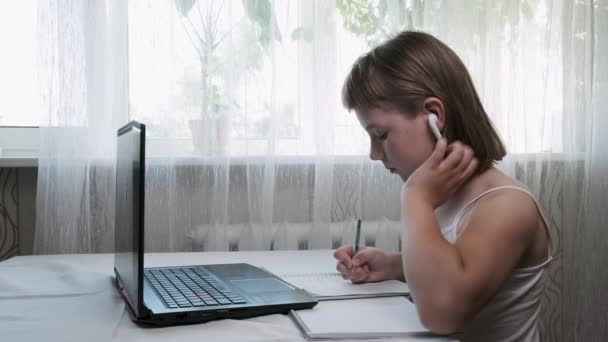 pieni tyttö kuulokkeissa, tutkimukset kotona internet-opettajan kanssa kannettavan tietokoneen kautta - Materiaali, video