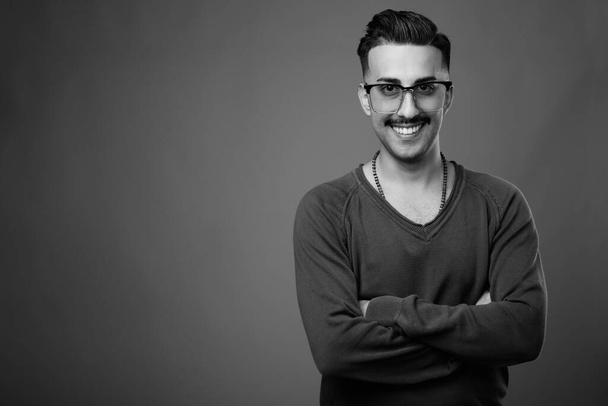 Studio shot młodego przystojnego Irańczyka z wąsami z długim rękawem na szarym tle w czerni i bieli - Zdjęcie, obraz