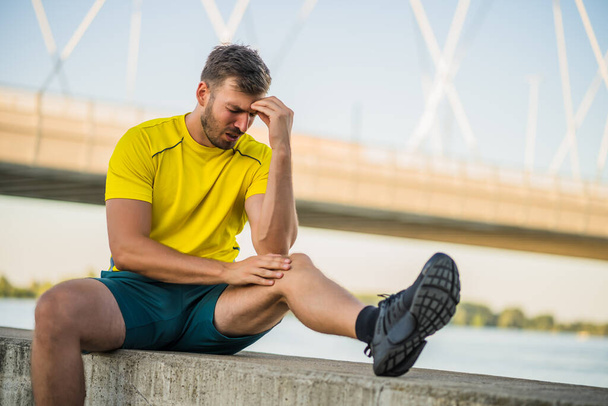 Giovane uomo sta avendo dolore al ginocchio durante l'esercizio e il jogging all'aperto. - Foto, immagini