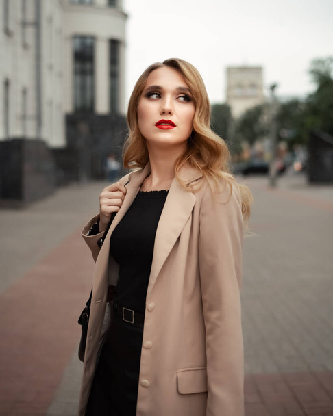 Portrait of young beautiful woman with long blonde hair in beige trench coat with a bag on the city street. People lifestyle concept - Foto, Imagen