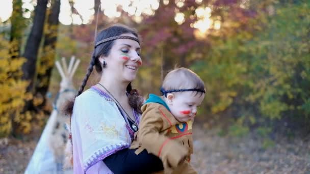 Donna con bambino gioca in costumi nativi americani e indiani nel parco in autunno. Intrattenimento elegante nel parco. Giornata del patrimonio dei nativi americani. - Filmati, video