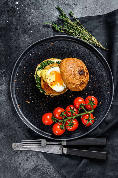 Delicious fishburger with fish fillet, egg and spinach on a brioche bun. Black background. Top view. - Foto, Imagen