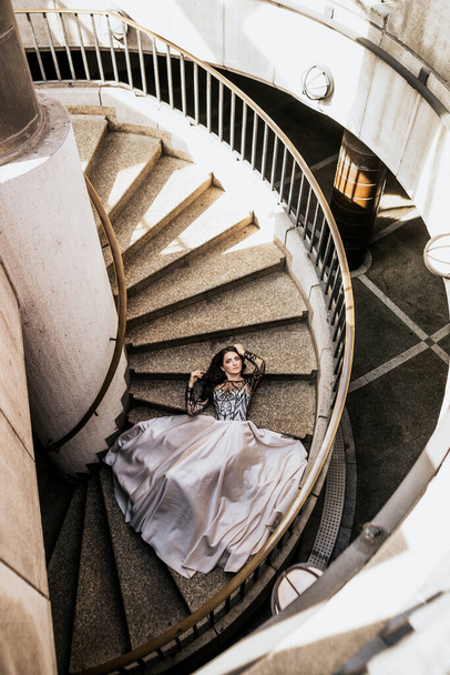 Piękna atrakcyjna kobieta leżąca na schodach w białej czarnej sukience. Widok z góry młodej kobiety wewnątrz budynku - Zdjęcie, obraz