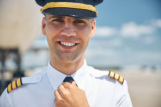 Χαρούμενος πιλότος στη διοίκηση προσαρμόζει τη γραβάτα του στο αεροδρόμιο. - Φωτογραφία, εικόνα