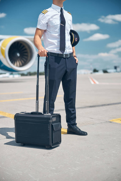 Piloto masculino con maleta de viaje parado al aire libre en el aeródromo - Foto, Imagen